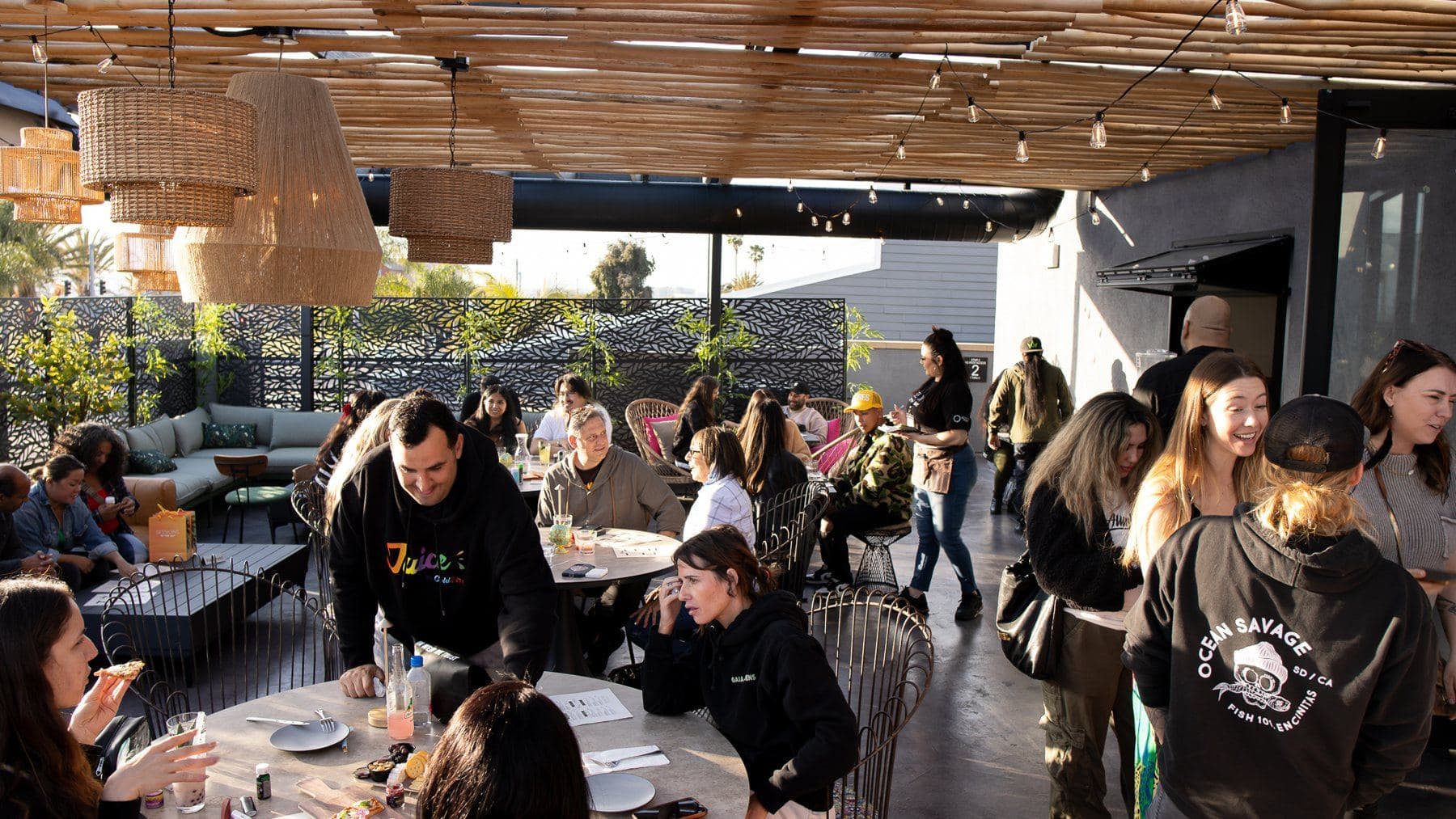 Guests at tables on the patio under string lights in late afternoon sun